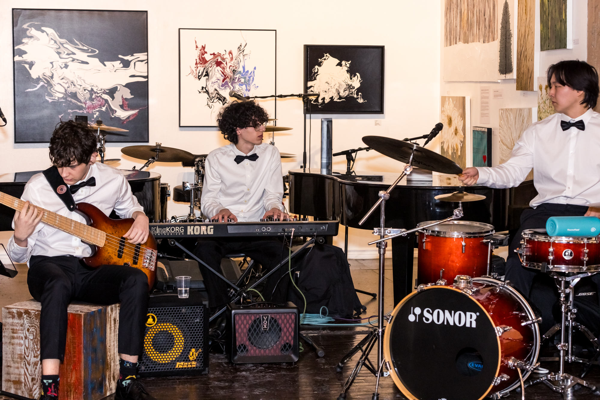 A live trio of bass, keyboard and drums creating atmosphere at a gallery event